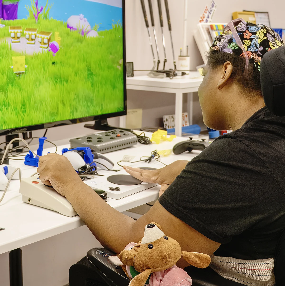 A person in a wheelchair using an adaptive controller to play a video game on a large screen