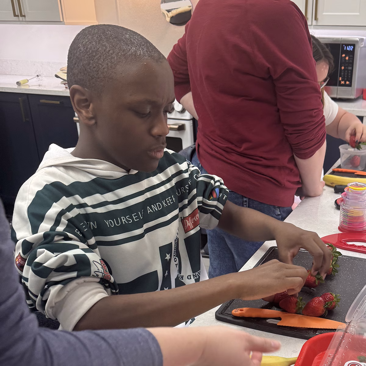 A young person in a striped hoodie preparing strawberries in a kitchen A young person in a striped hoodie preparing strawberries in a kitchen
