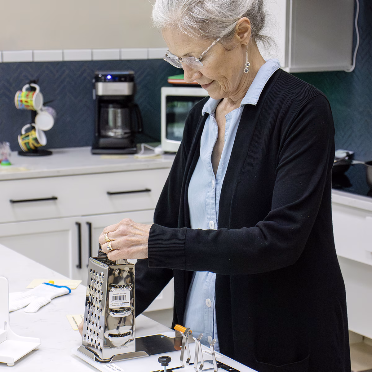 An older adult using an Assistive Technology grater in a kitchen An older adult using an Assistive Technology grater in a kitchen