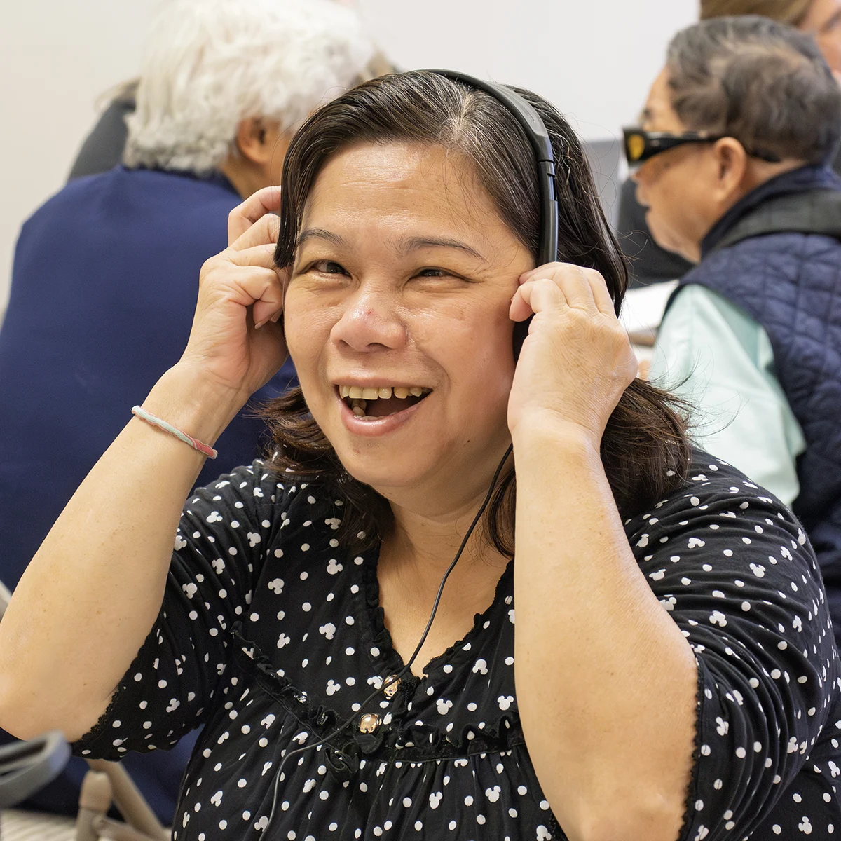 An older woman smiling and wearing headphones for a personal amplifier