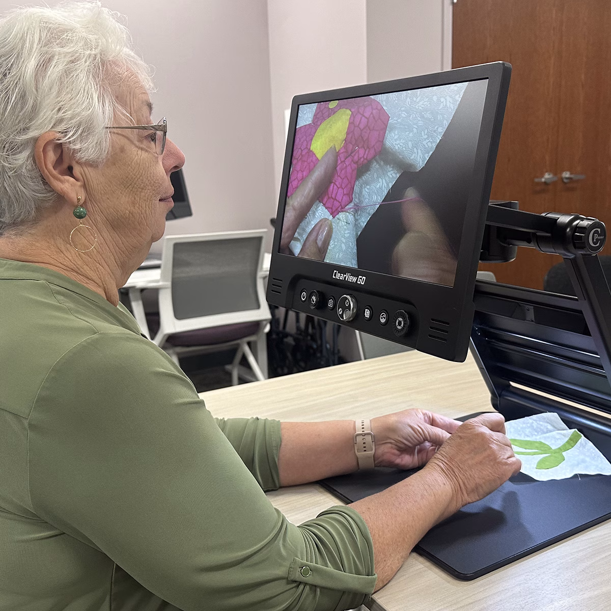 An older woman uses a magnification device to sew on fabric An older woman uses a magnification device to sew on fabric