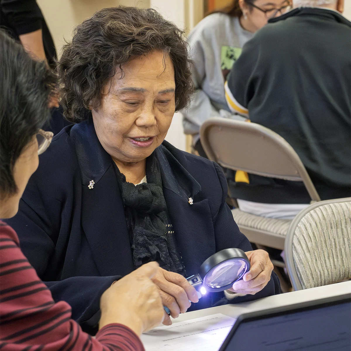 Elderly woman using a magnifying glass to view documents on a table