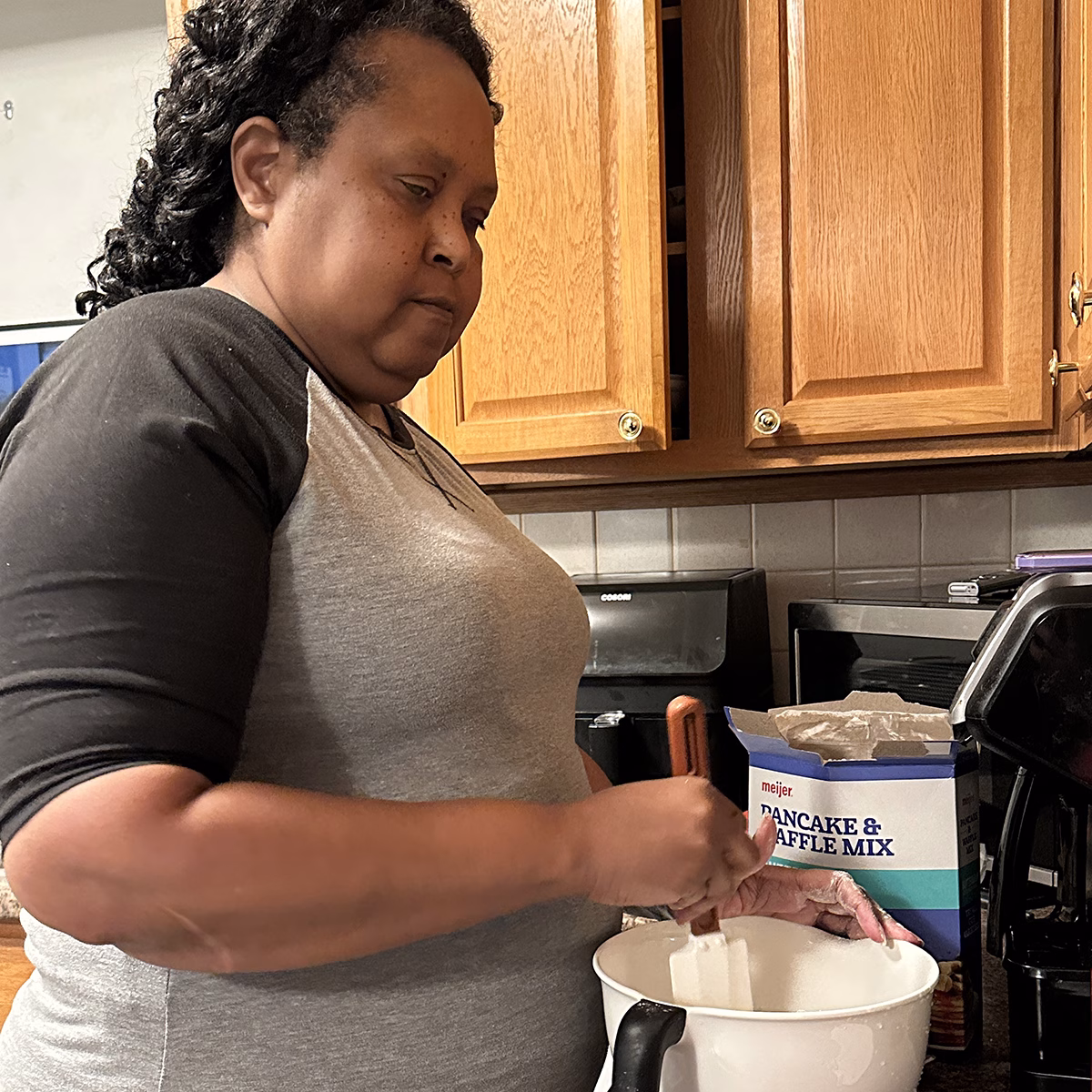 Person mixing ingredients in a kitchen with a box of pancake and waffle mix on the counter Person mixing ingredients in a kitchen with a box of pancake and waffle mix on the counter
