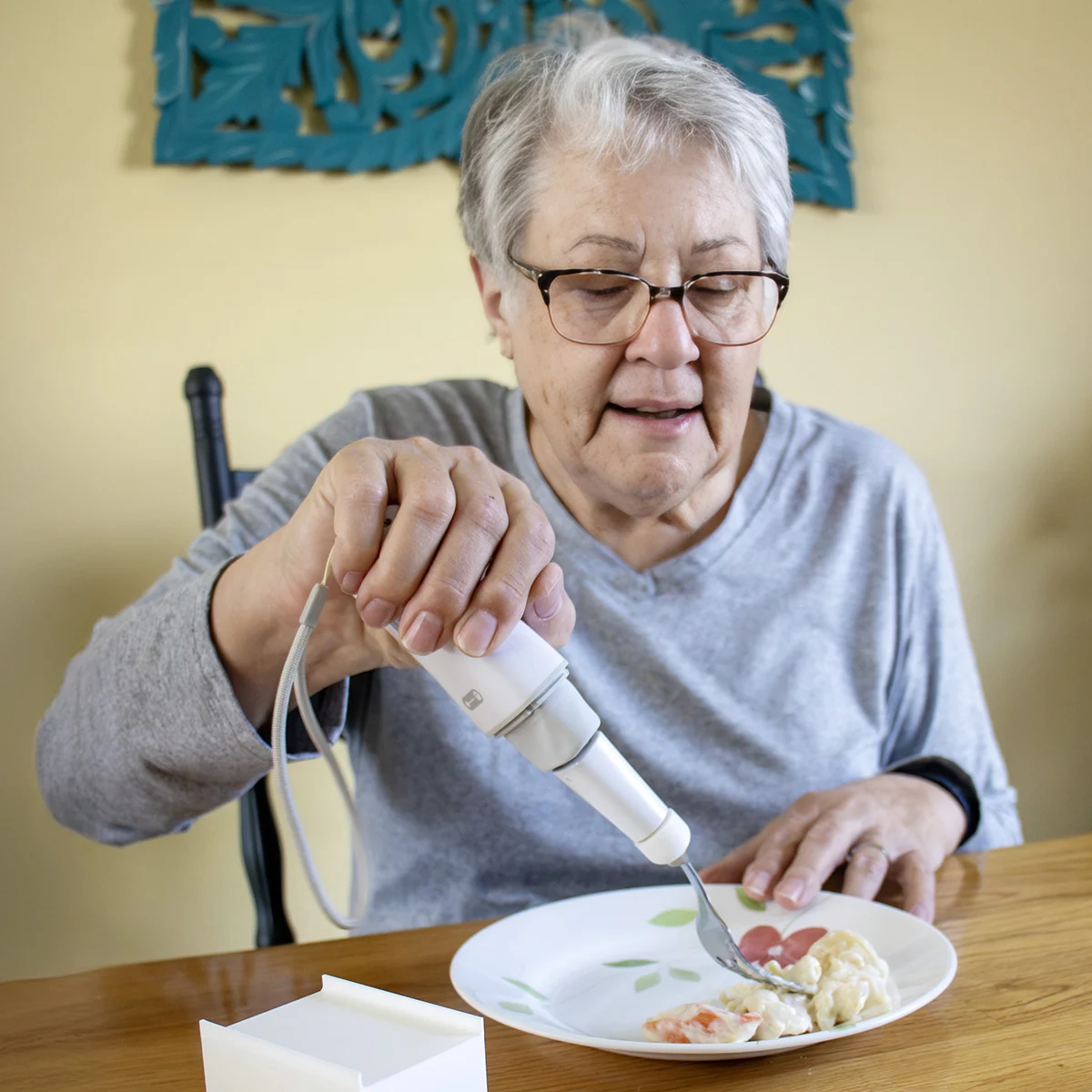 Person using an adapted spoon to eat from a white plate on a table