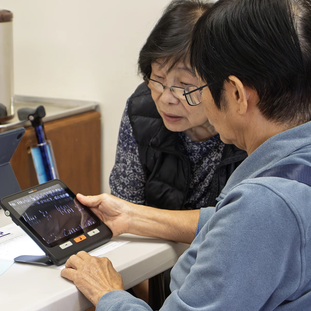 Two older adults examining a small magnifier to read text