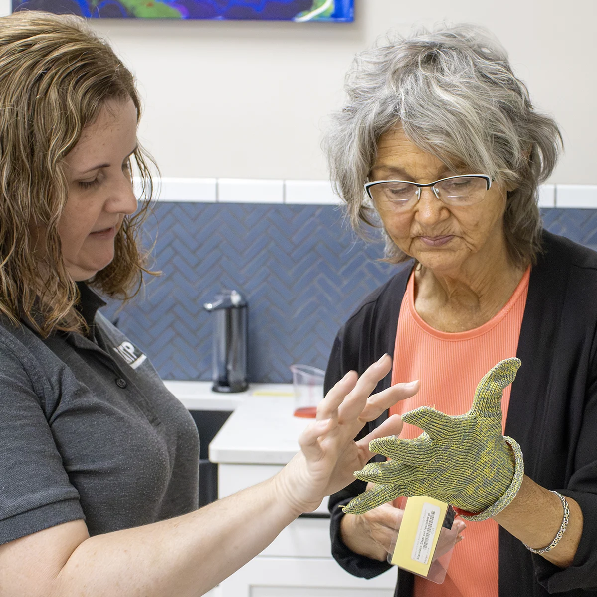 Two women examining a textured glove in a kitchen