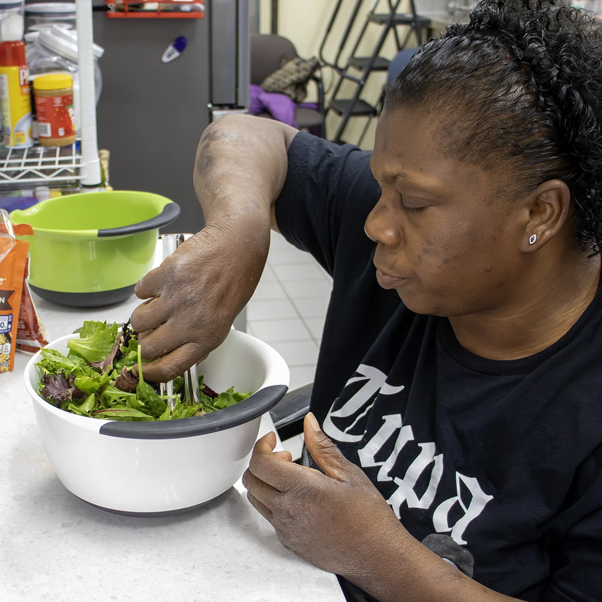 Woman mixing a salad in a non slip bottom bowl tongs in a kitchen