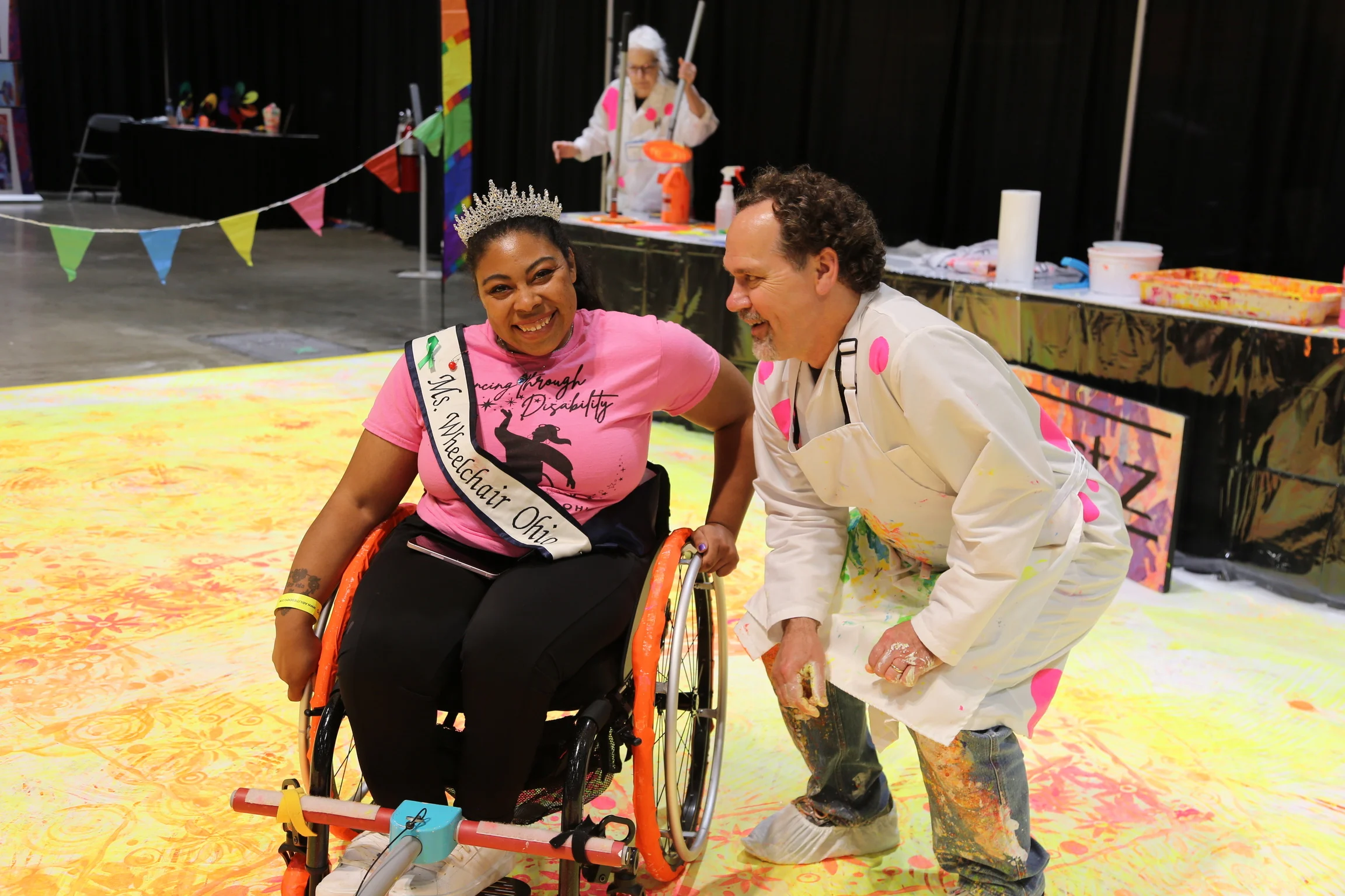 Woman in a wheelchair with an instructor wearing a painter's smock