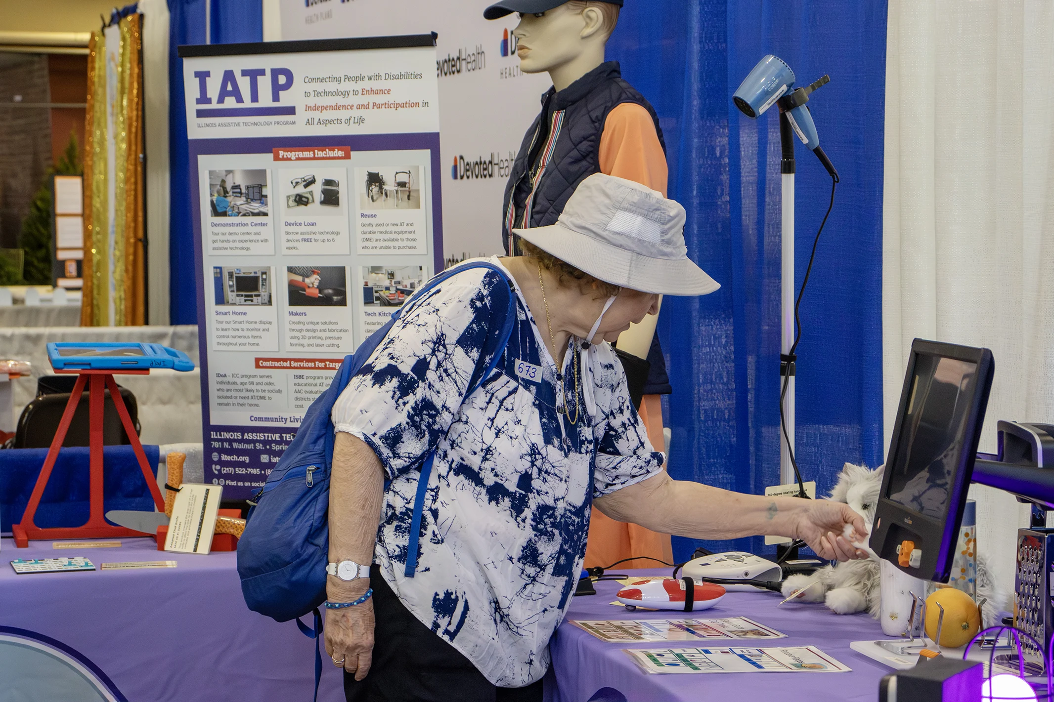 A woman explores assistive technology devices on a purple table at IATP’s booth.