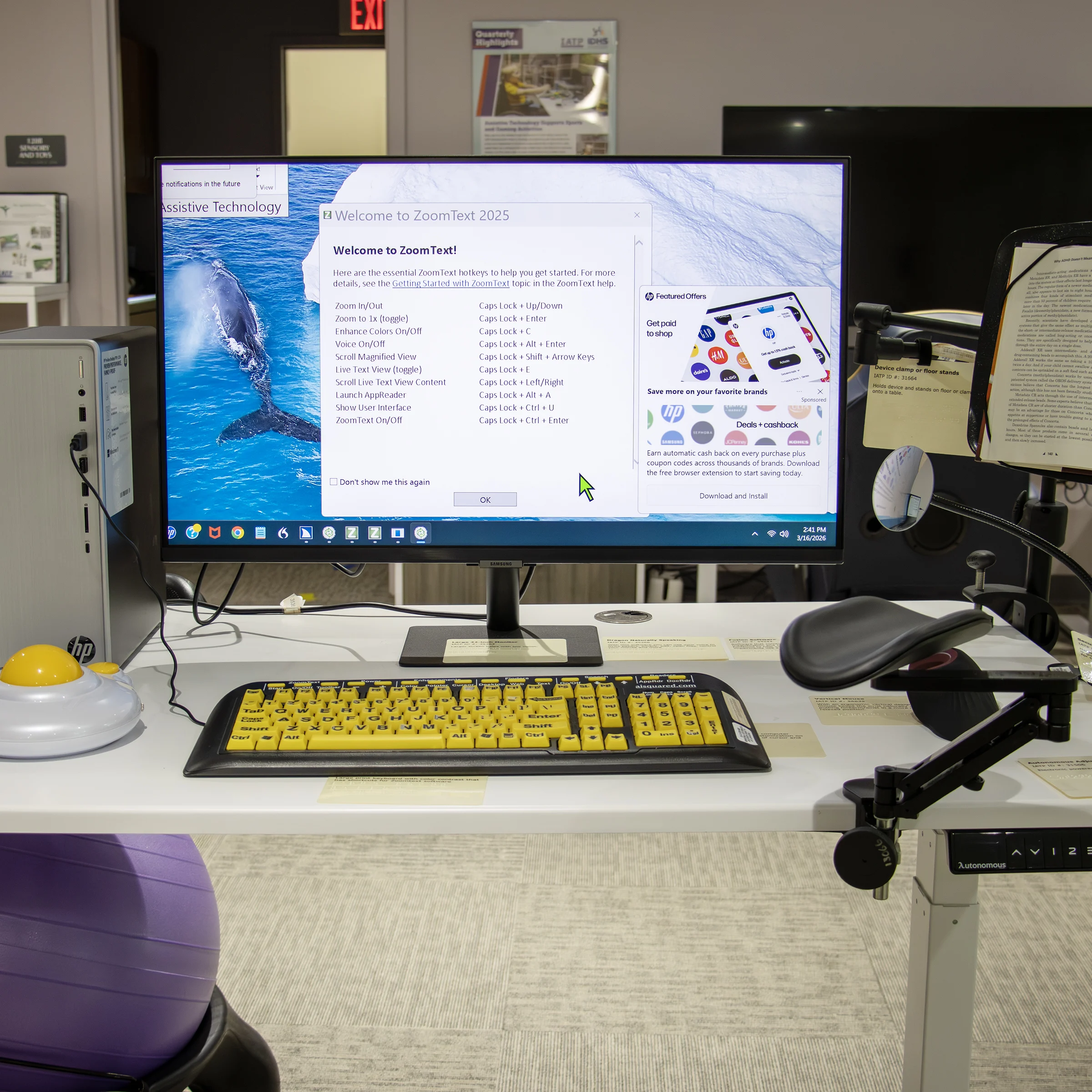 Computer workstation with a monitor displaying ZoomText software, a black and yellow keyboard, and a large trackball mouse in IATP’s Demonstration Center.