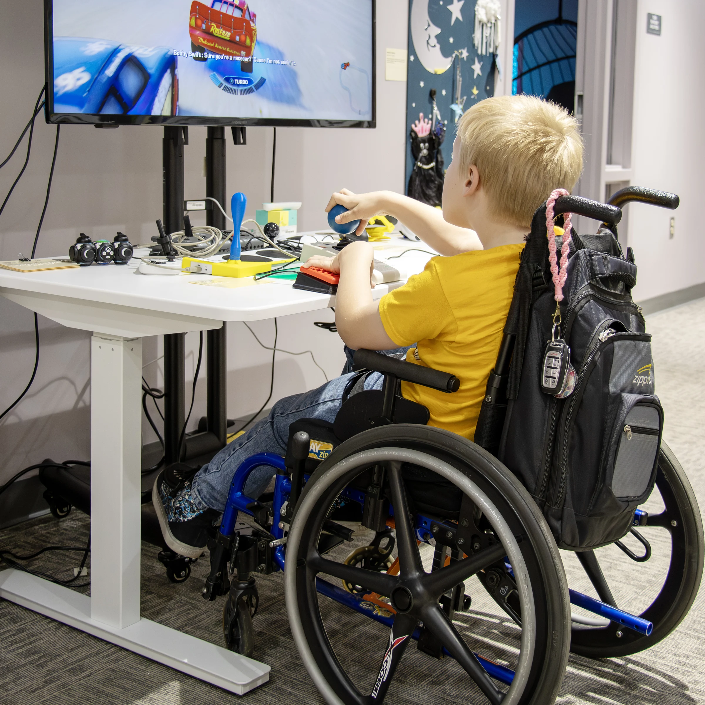 young child playing a video game while sitting in a wheelchair using adaptive gaming controls in IATP’s Demonstration Center.