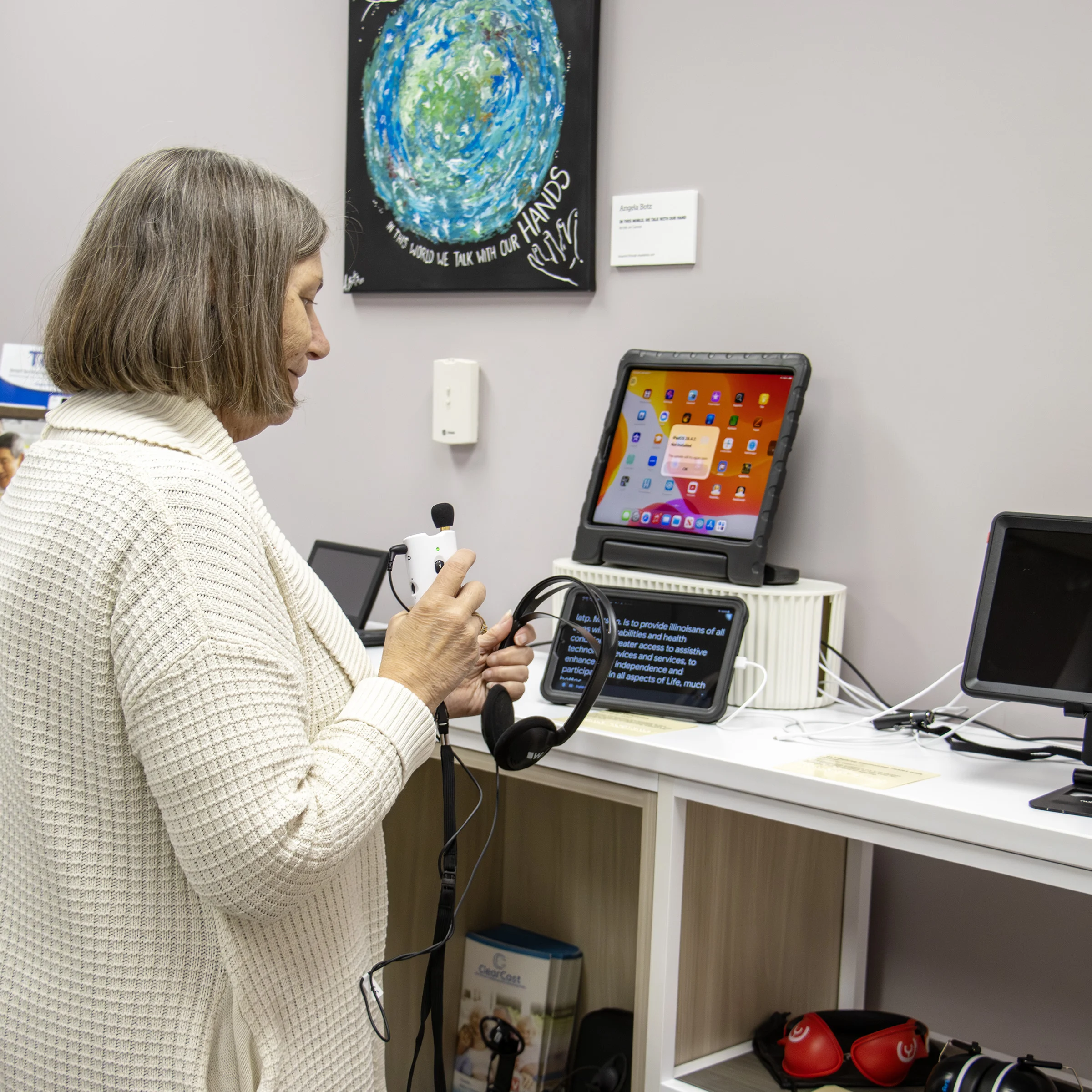 a person holds a headset and microphone in front of electronic devices on a shelf in IATP’s Demonstration Center
