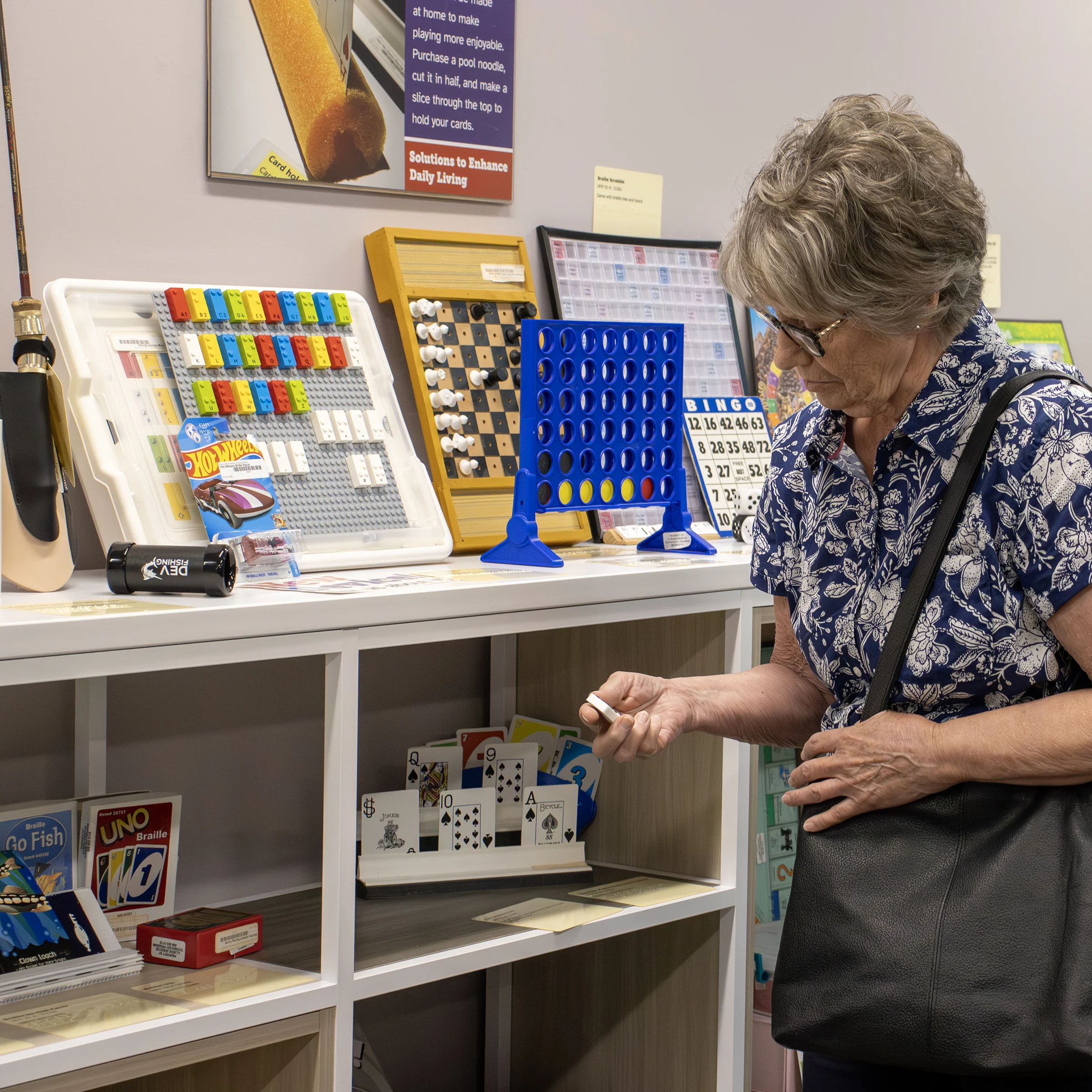 A person looking at accessible game piece with a shelf displaying various games and cards in IATP’s Demonstration Center