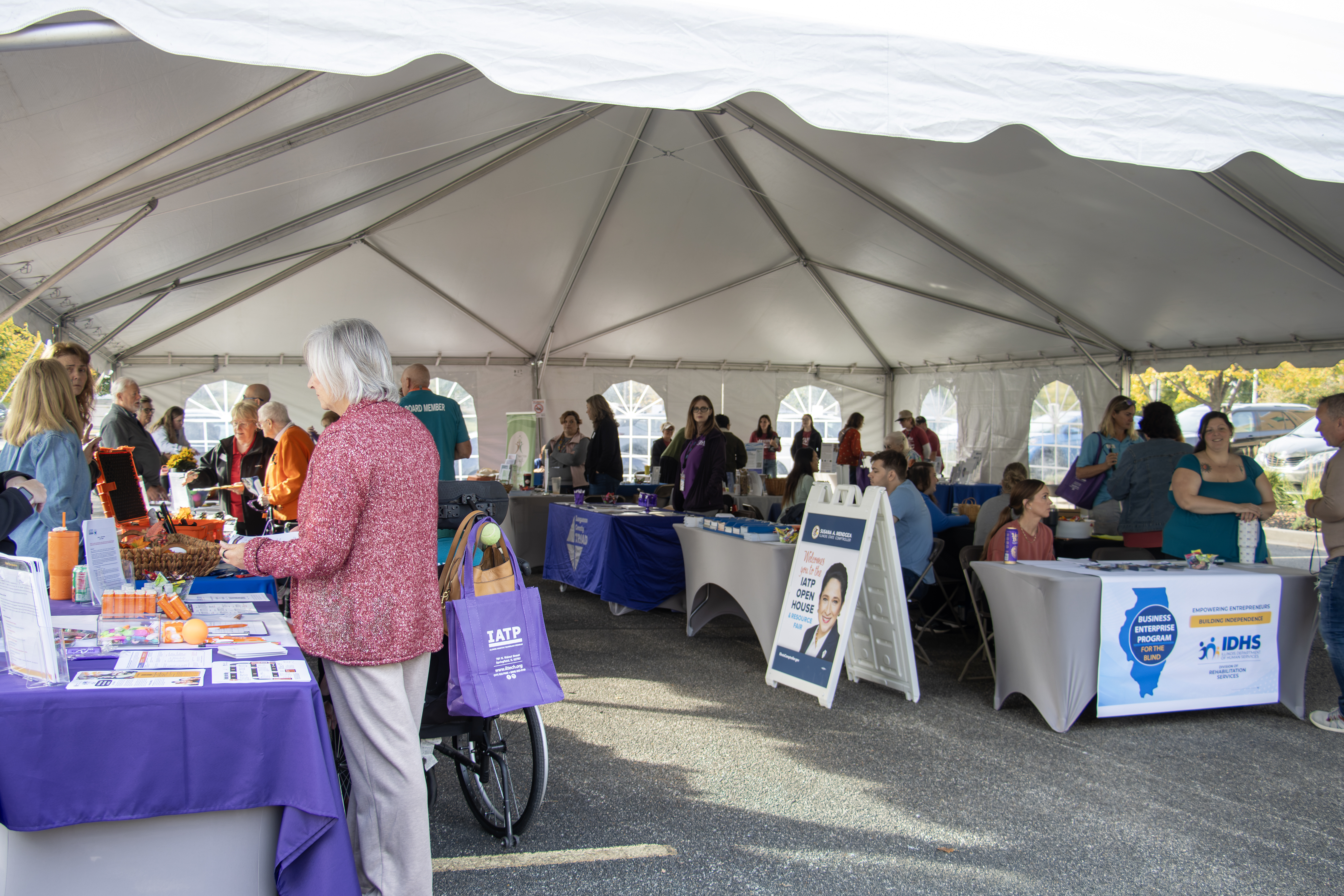 Open House People browse information booths at the IATP resource fair inside a large outdoor tent.