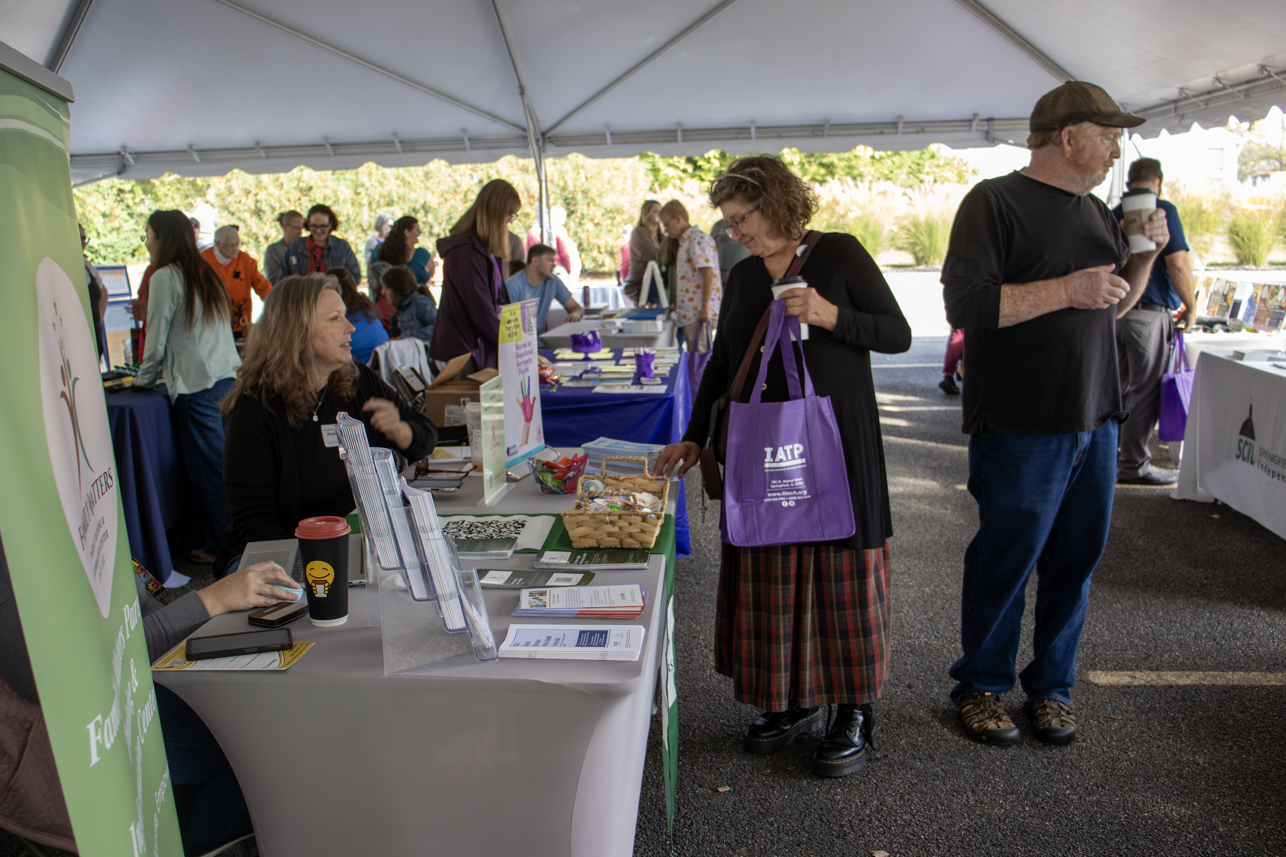 People browse informational booths the crowded outdoor IATP fair beneath a canopy