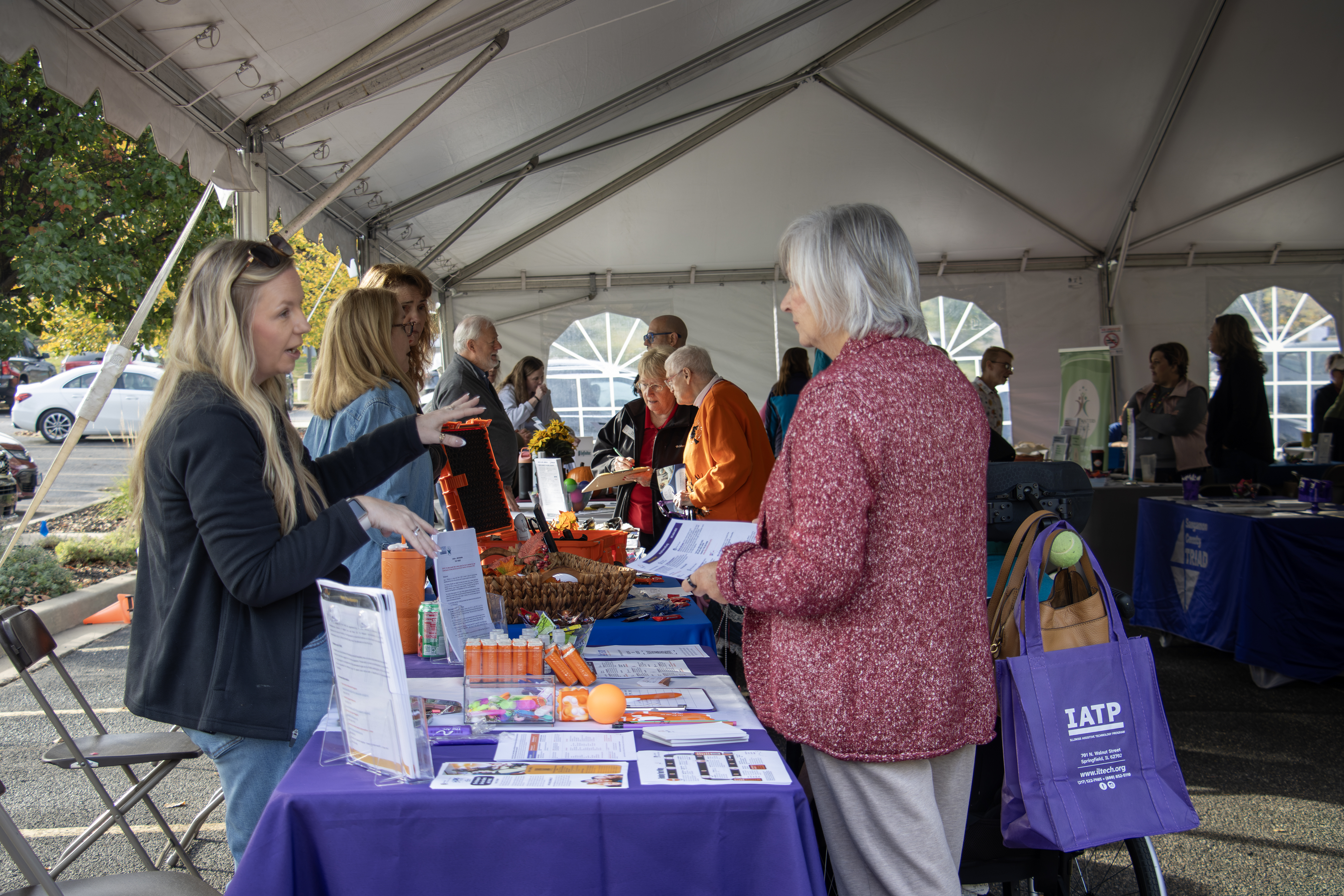 People gather at an information booth inside the outdoor event tent at IATP